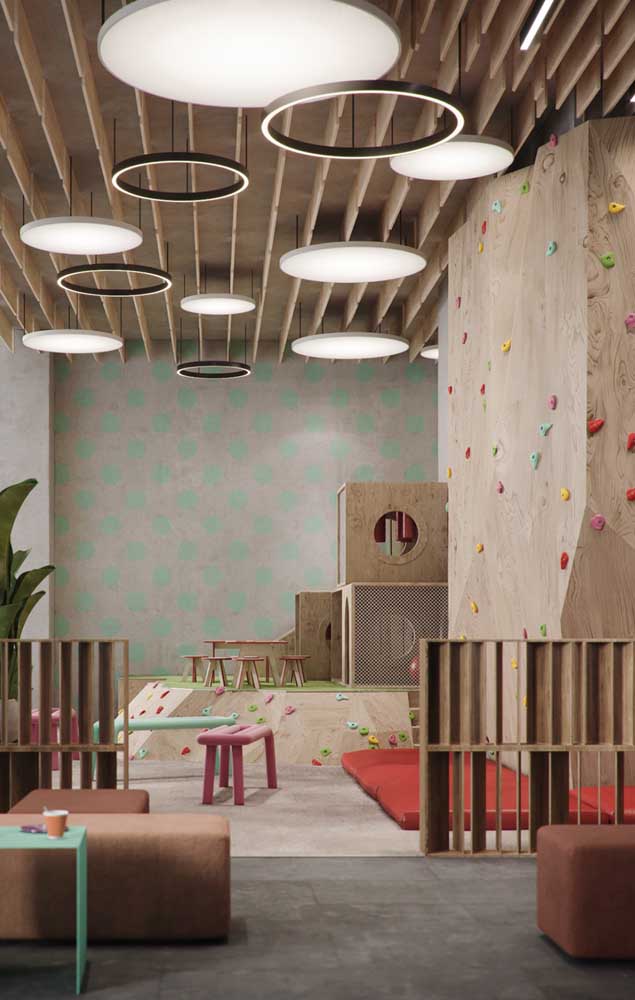 Aire de jeux intérieure avec mur d'escalade et maison en bois; remarquez les matelas placés sous le mur pour amortir les chutes possibles