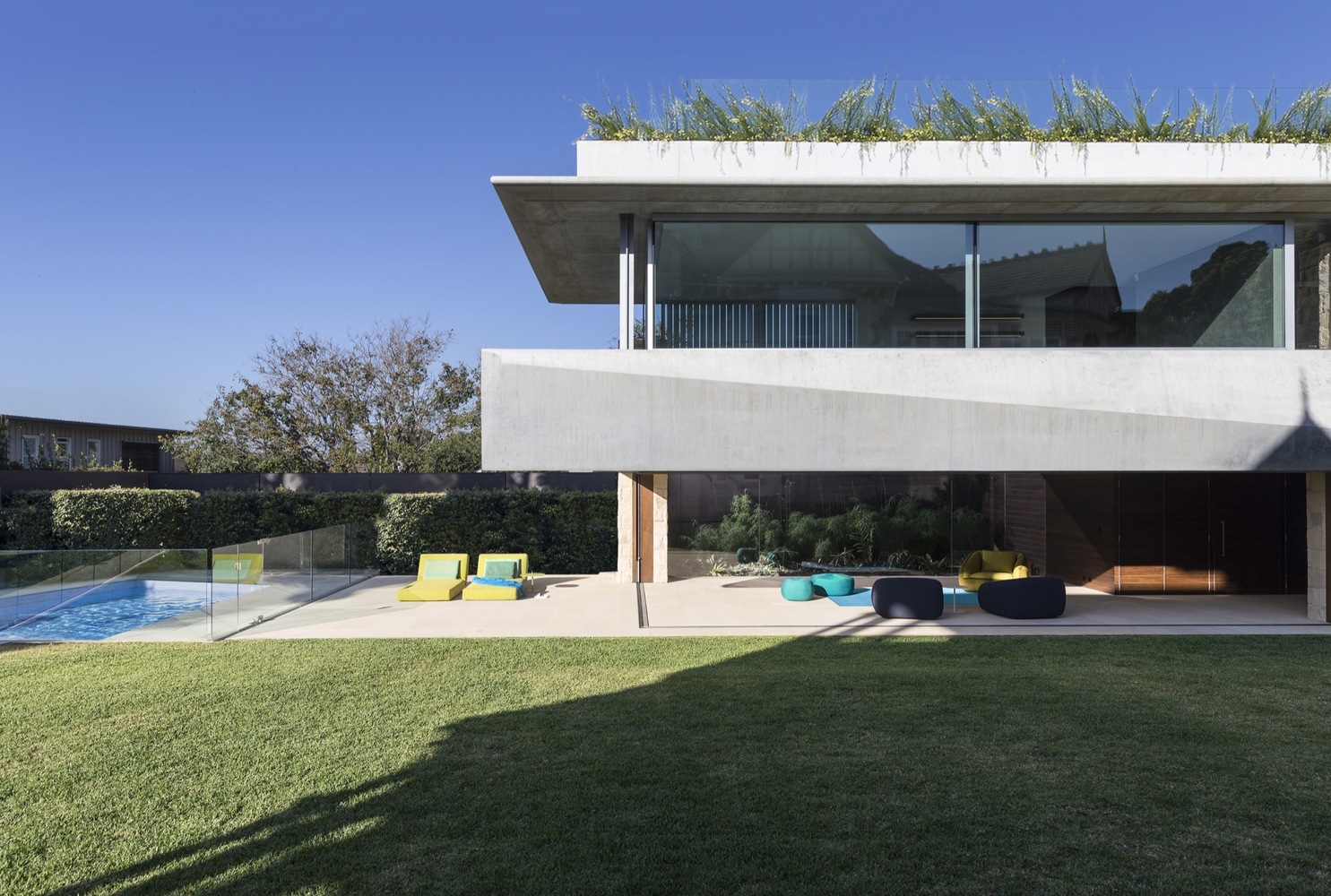 Espace extérieur de la maison de luxe avec piscine, espace vert et garde-corps en verre